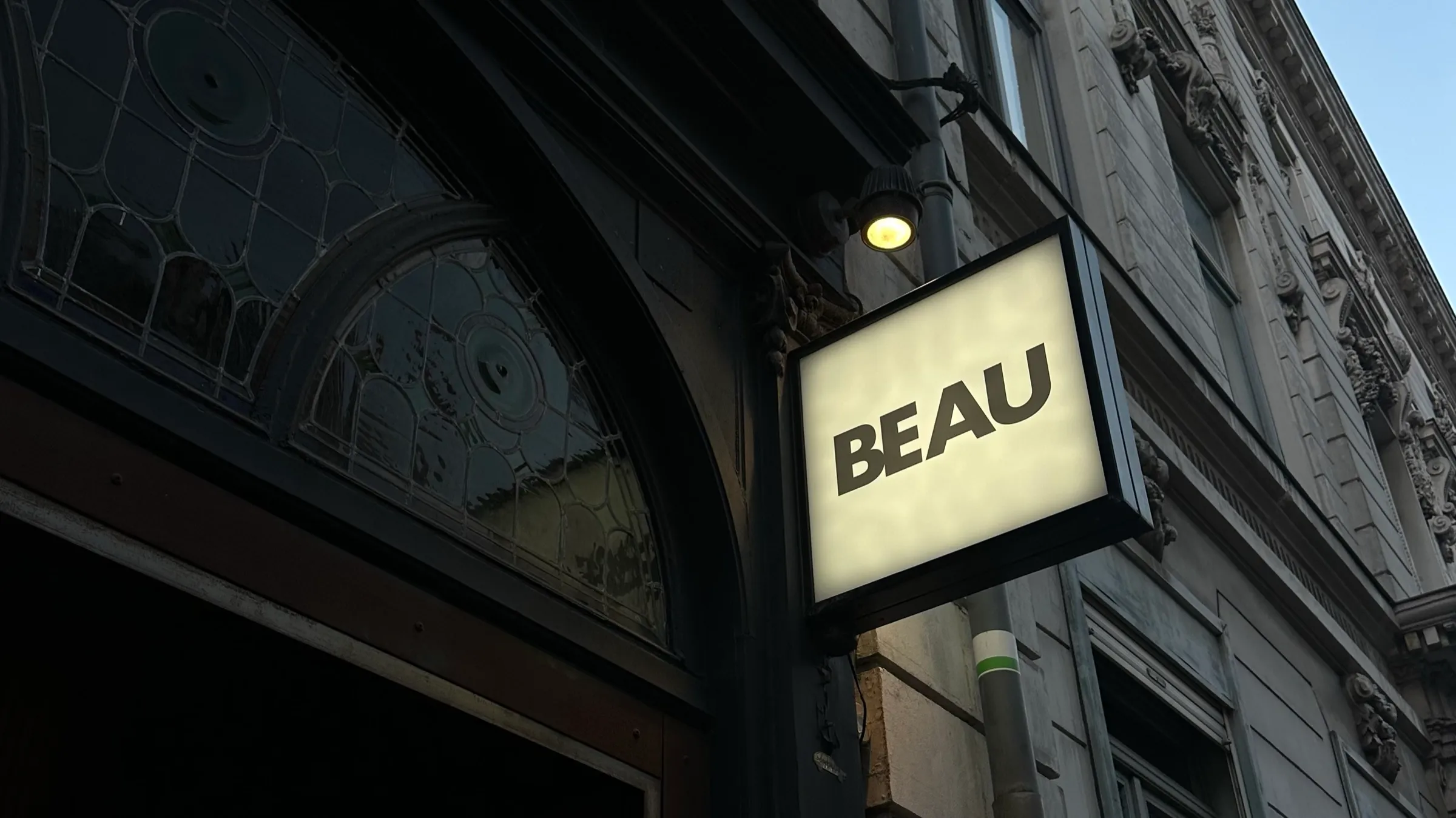 Enseigne lumineuse BEAU sur la façade noire du salon, rue Basse