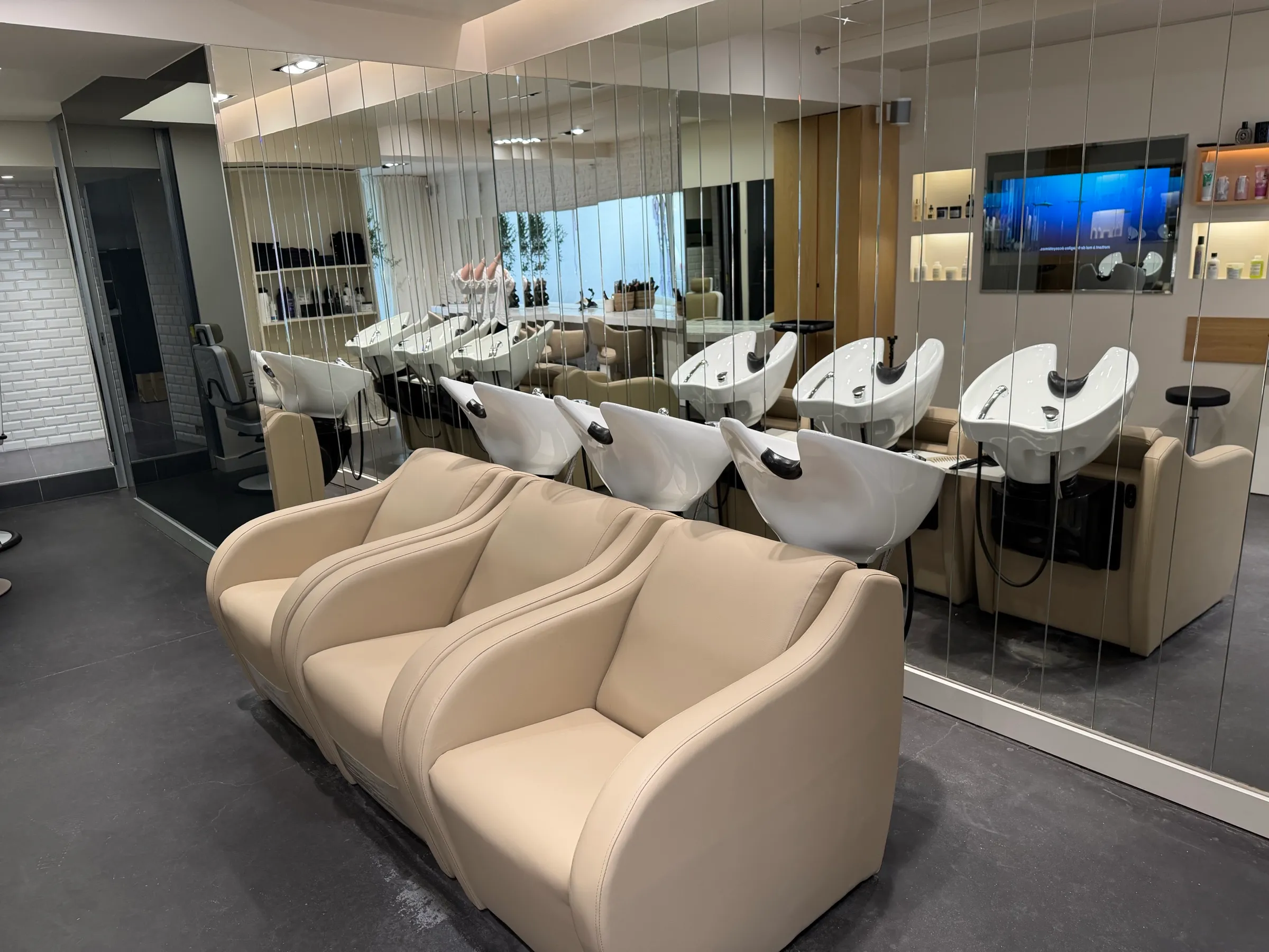 Espace shampoing de BEL.LE : fauteuils en cuir beige et bacs blancs devant un grand miroir