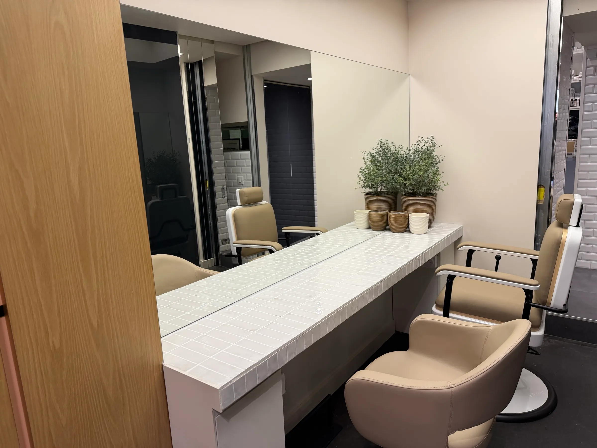 Poste de coiffage de BEL.LE avec plan carrelé blanc, plantes et fauteuil beige