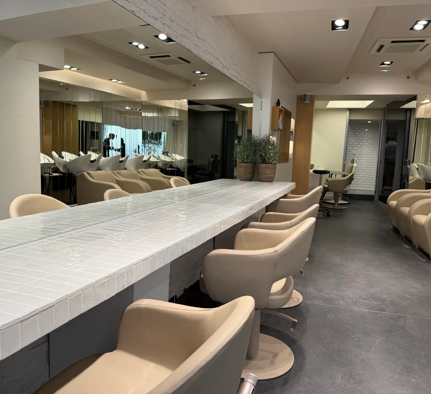 Intérieur de BEL.LE, salon de coiffure femme à Lille : long plan de travail carrelé blanc et fauteuils beiges